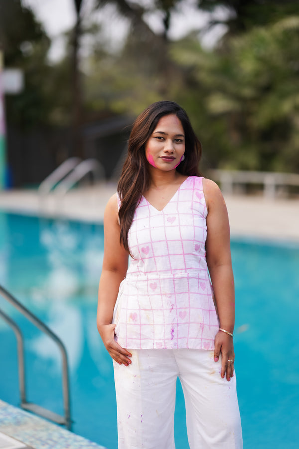 Woman standing by a pool wearing a pink sleeveless top and white pants.